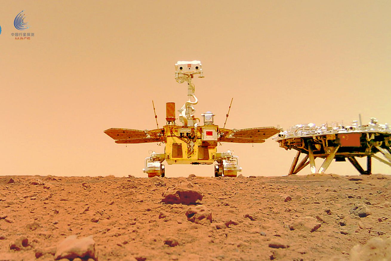 The rover sits in the center of the photo, which is angled upward from the red martian surface. To its right is the landing platform.