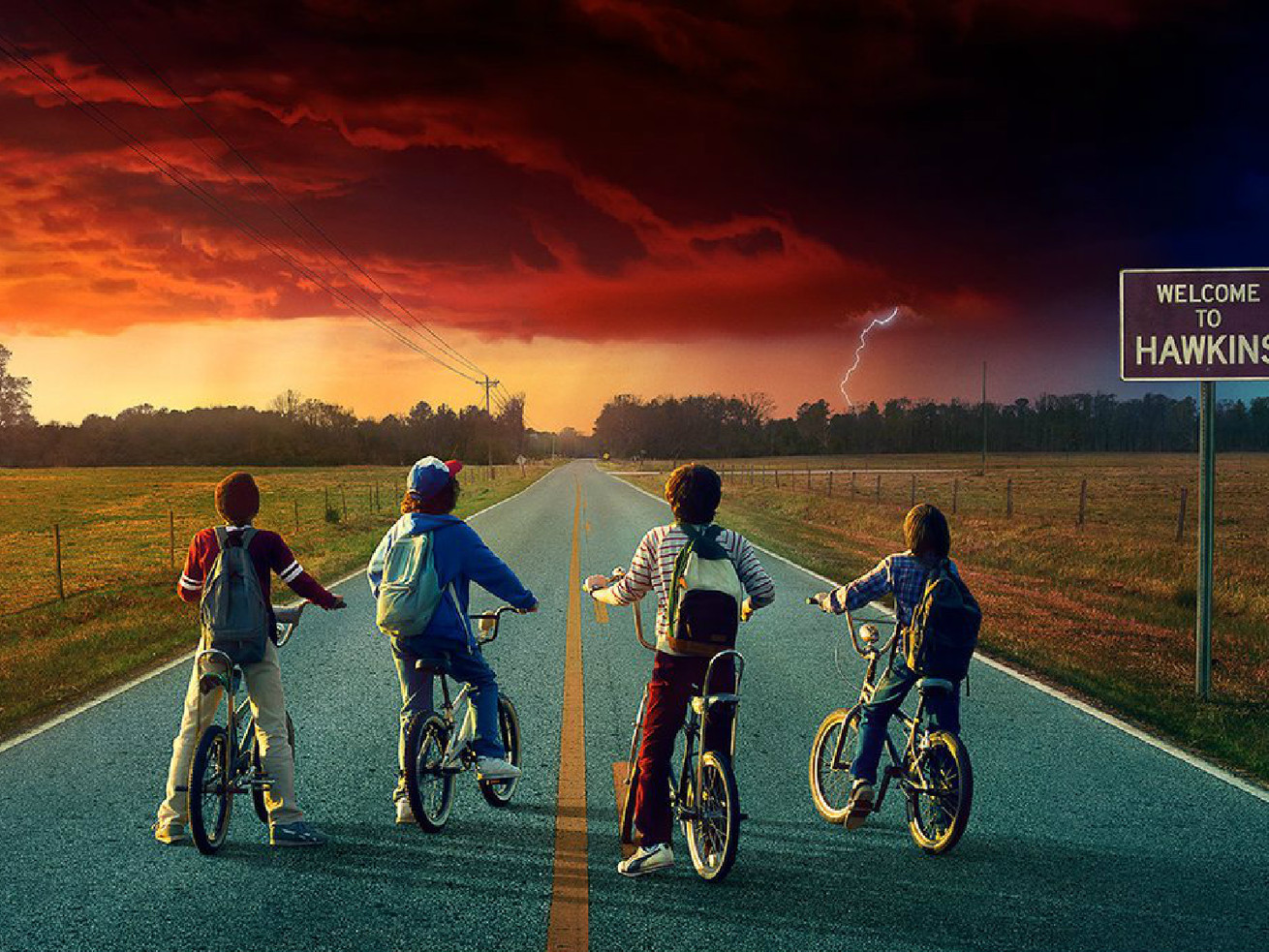 “Stranger Things 2” promo image of four boys on bikes, stopped on a paved road, looking at a threatening cloud on the horizon