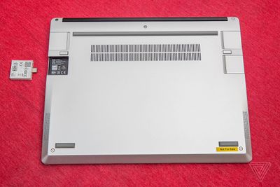 The Framework laptop closed, upside-down on a red tablecloth. One of its four port slots is empty. An expansion card sits beside the empty port, upside-down with its QR code facing up.