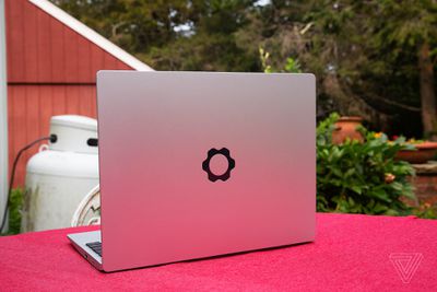 The Framework Laptop in a garden on top of a red tablecloth, facing away from the camera, open, angled to the left.